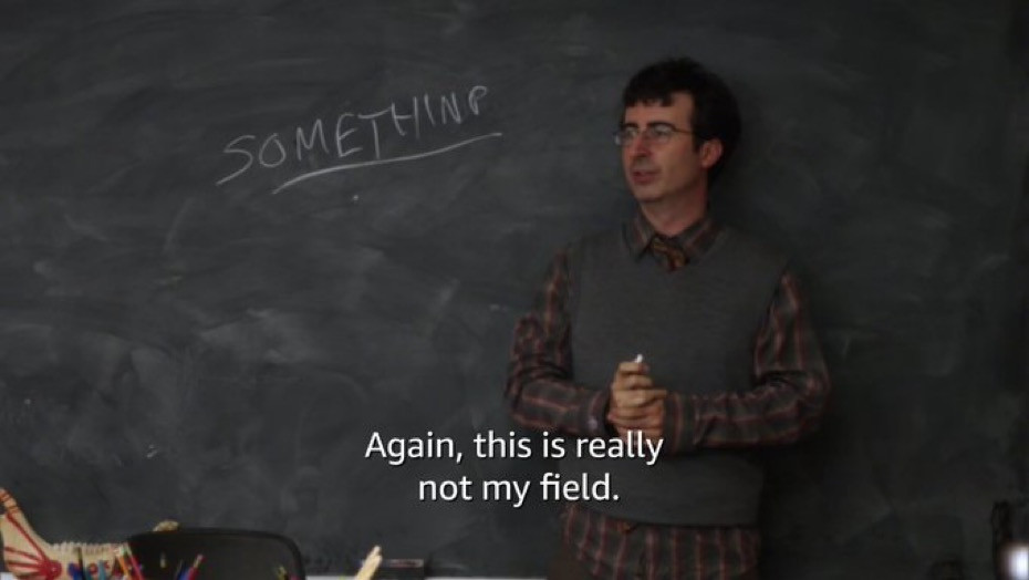 Jon Oliver as professor Ian Duncan. He wears a plaid shirt with a sweater vest over it and it a middle aged white man wearing glasses and with a short but scruffy haircut. He's standing in front of a chalkboard that says, "something" and is saying "Again, this is really not my field."